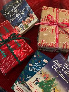 four wrapped presents sitting on top of a red blanket next to books and a cell phone