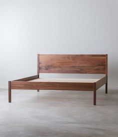 a wooden bed frame sitting on top of a cement floor next to a white wall