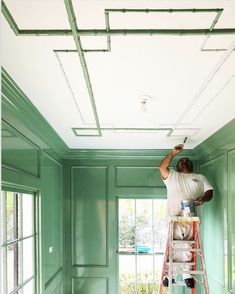 a man on a ladder painting the ceiling in a room with green walls and white trim