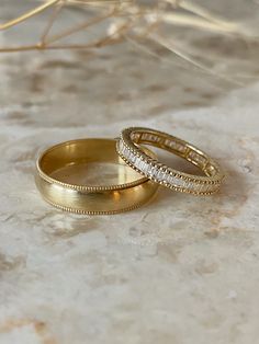 Vintage-inspired wedding bands in yellow gold stacked. Rounded men's band with a brush finish and milgrain texture detailing along the borders. Women's wedding band is an eternity channel set style with baguette diamonds vertically set between a similar milgrain texture detailed border for a matching wedding band set. Wedding Rings His, Simple Elegant Rings Gold, Wedding Band Mixed Metals, Wedding Bands Men And Women, Simple Wedding Band Set, Roman Numeral Wedding Band, Gold Wedding Band Sets His And Hers, Wedding Bands His And Hers Gold, Wedding Ring Gold And Silver