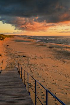 a wooden walkway leading to the beach at sunset