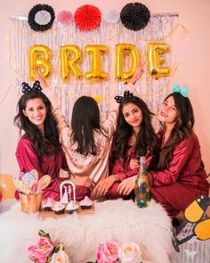 three women in matching robes sitting at a table with balloons and streamers on the wall behind them