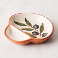 an orange and white bowl with olives painted on the side, sitting on a marble surface