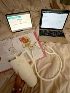 an open laptop computer sitting on top of a bed next to a book and cup