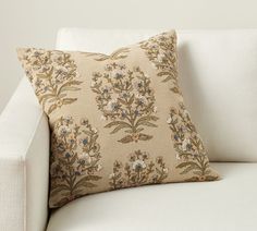 a white couch with a floral pillow on it's backrest and the arm rest down