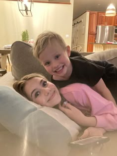 two children are laying on a couch with their arms around each other and smiling at the camera