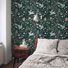 a bed sitting under a lamp next to a wall with birds and flowers on it