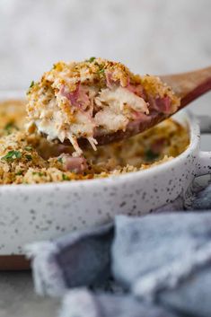 a wooden spoon is lifting up some food from a casserole dish with meat and cheese