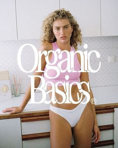 a woman in a pink top and white panties standing next to a counter with the words organic basics on it