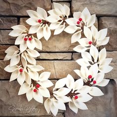 a wreath with white flowers and red berries hanging on a stone wall in front of a brick wall