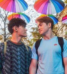 two young men are standing under umbrellas in the rain, looking at each other