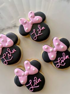 four decorated cookies with pink bows and name written on them in the shape of minnie mouses