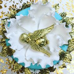 a gold and white flower with an angel brooch on it's center piece