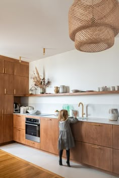 a woman standing in a kitchen next to a counter top oven and sink under a wicker light fixture