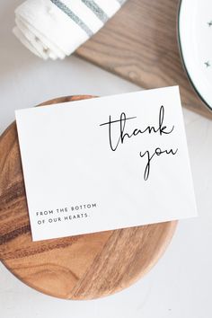 a thank you card sitting on top of a wooden plate next to a white napkin