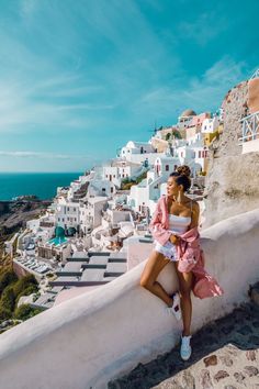 a woman sitting on top of a white wall next to the ocean