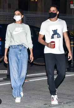 a man and woman walking down the street wearing face masks