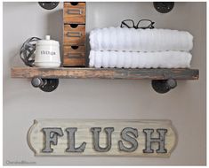 a bathroom shelf with towels and eyeglasses on it, next to a wooden sign that says flush