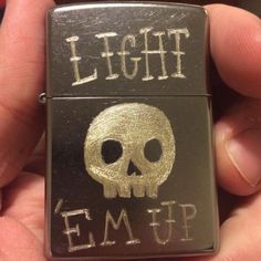 a lighter with a skull on it that says light em up in white ink and gold foil