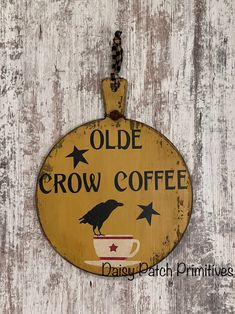 an olde crow coffee sign hanging on a white wooden wall with a black bird perched on the cup