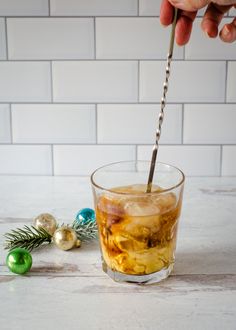 a person is holding a straw in a glass with ice and christmas decorations on the side