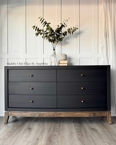 a black dresser with gold handles and drawers in front of a white paneled wall