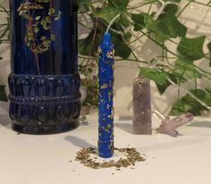 a blue vase sitting on top of a white table next to a candle and some plants