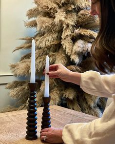 a woman is holding two candles in front of a fake christmas tree that has been placed on the table