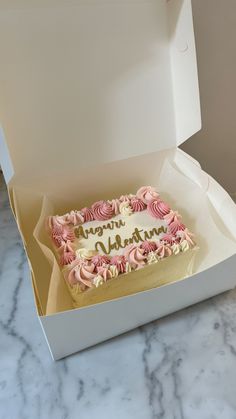 a birthday cake in a box on a marble counter top with white and pink frosting