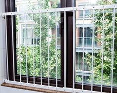 an open window with bars on it in front of a white wall and trees outside