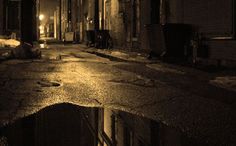 an empty city street at night with puddles on the ground and buildings in the background