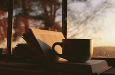 an open book and coffee cup sitting on a window sill