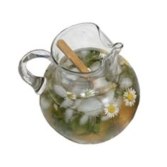 a glass pitcher filled with water and flowers on top of a white table next to a wooden spoon