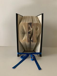 an open book with blue ribbon around it and the pages folded to look like a man's face