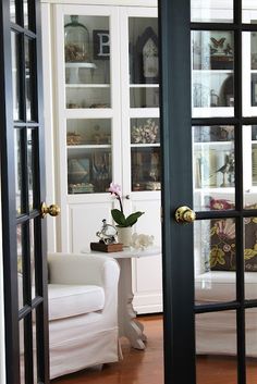 an open door leading to a living room with white furniture and flowers in vases