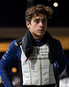 a young man with his hands on his hips looking at the camera while wearing a racing suit