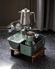 a green coffee maker sitting on top of a wooden stand with pots and pans