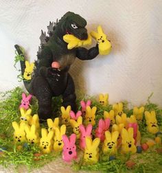 there are many small toy animals in the grass with one godzilla holding an egg and another is eating