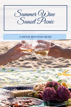 two people toasting wine glasses on the beach with food and flowers in front of them