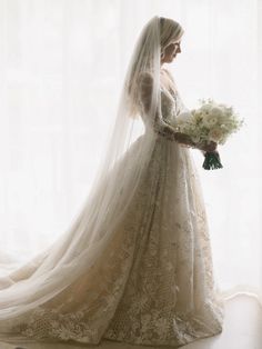 a woman in a wedding dress is standing by a window with her veil pulled back