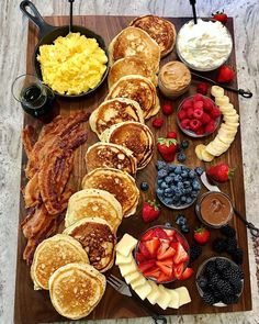 pancakes, fruit, and other breakfast foods are arranged on a cutting board