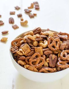 a bowl filled with nuts and pretzels on top of a white table next to pecans