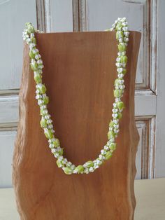 a green and white beaded necklace sitting on top of a wooden stand in front of a door