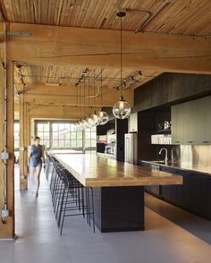 a large kitchen with an island and bar stools in the center, while two people walk past it