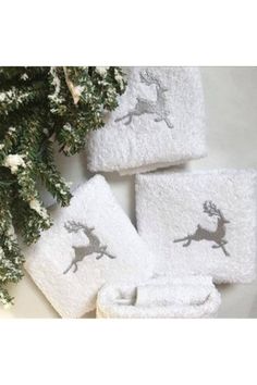 four white towels with deers on them next to a tree and snowflakes