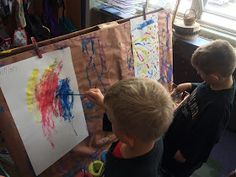 two young boys are painting on an easel