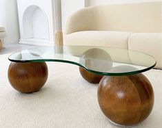 a glass and wood coffee table in the middle of a living room with white carpet