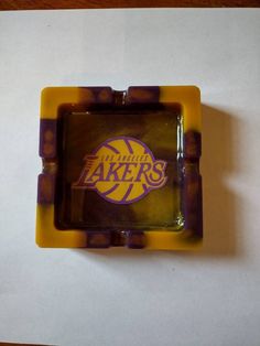 the los angeles lakers logo is on top of a yellow and purple plastic object that sits on a white sheet of paper