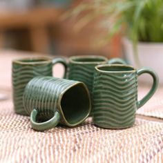 three green coffee mugs sitting on top of a table next to a potted plant