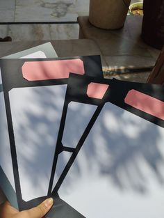 a person holding three pieces of paper with pink and black strips on them, in front of a table